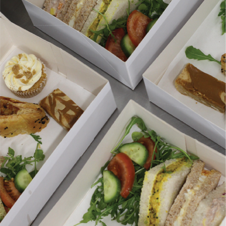 A selection of sandwiches and snacks in takeaway boxes, featuring fresh salad and sandwich fillings, ready for corporate lunches.