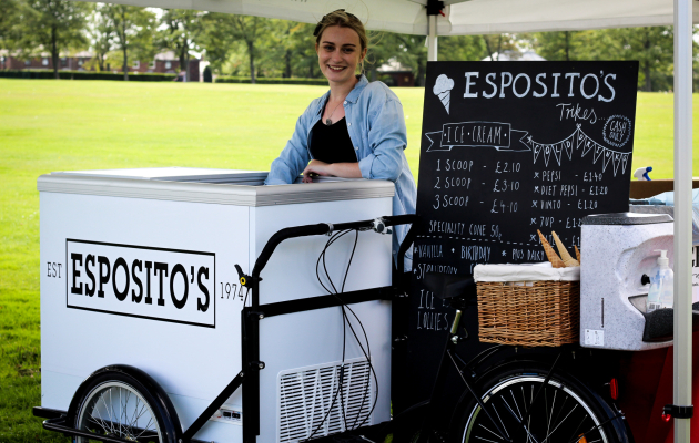 Friendly staff serving ice cream from an Esposito's cart at an outdoor event, with pricing board for various flavours