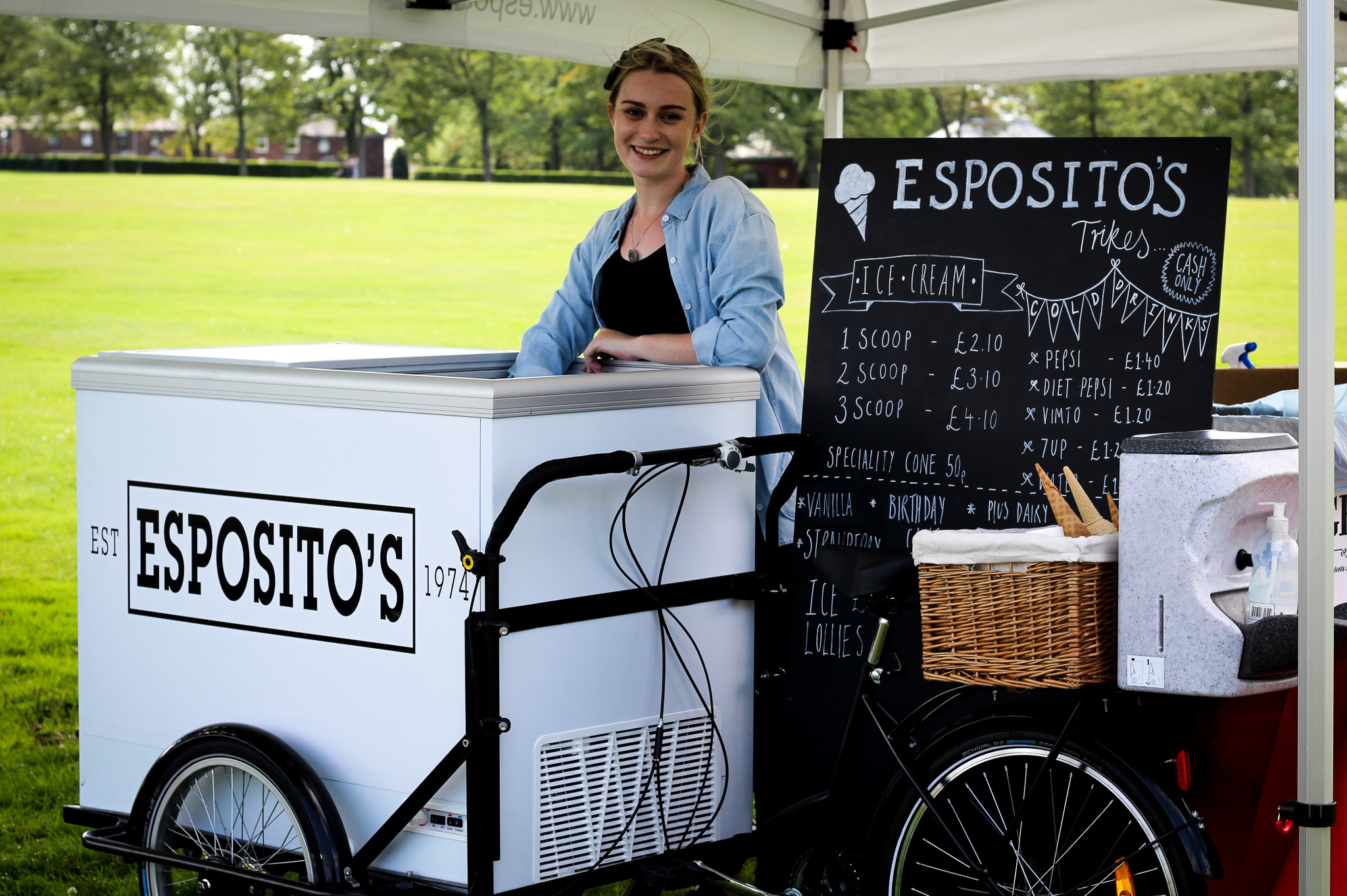 Friendly staff serving ice cream from an Esposito's cart at an outdoor event, with pricing board for various flavours